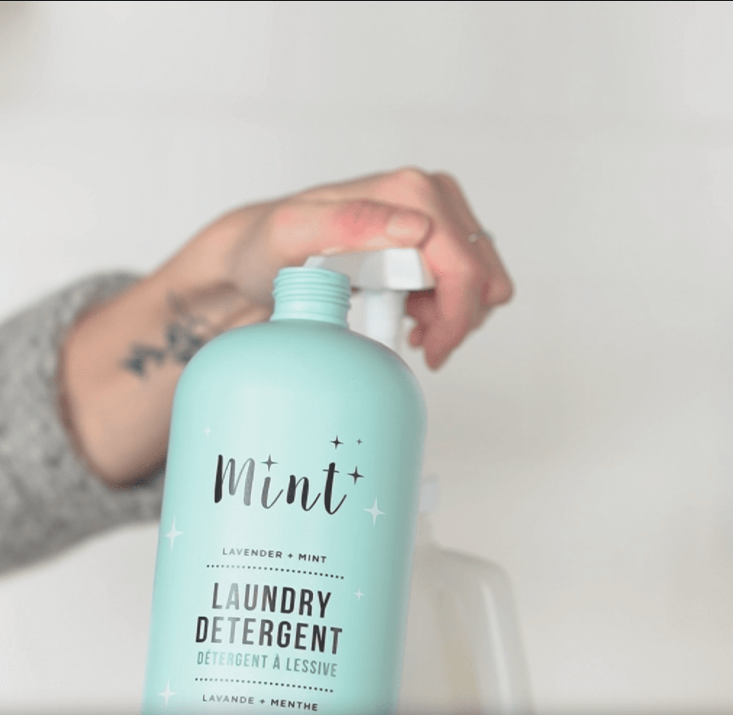 A person refills an empty laundry detergent bottle using the Mint Cleaning Products laundry detergent refill jug, showing a straightforward and eco-friendly refill process.