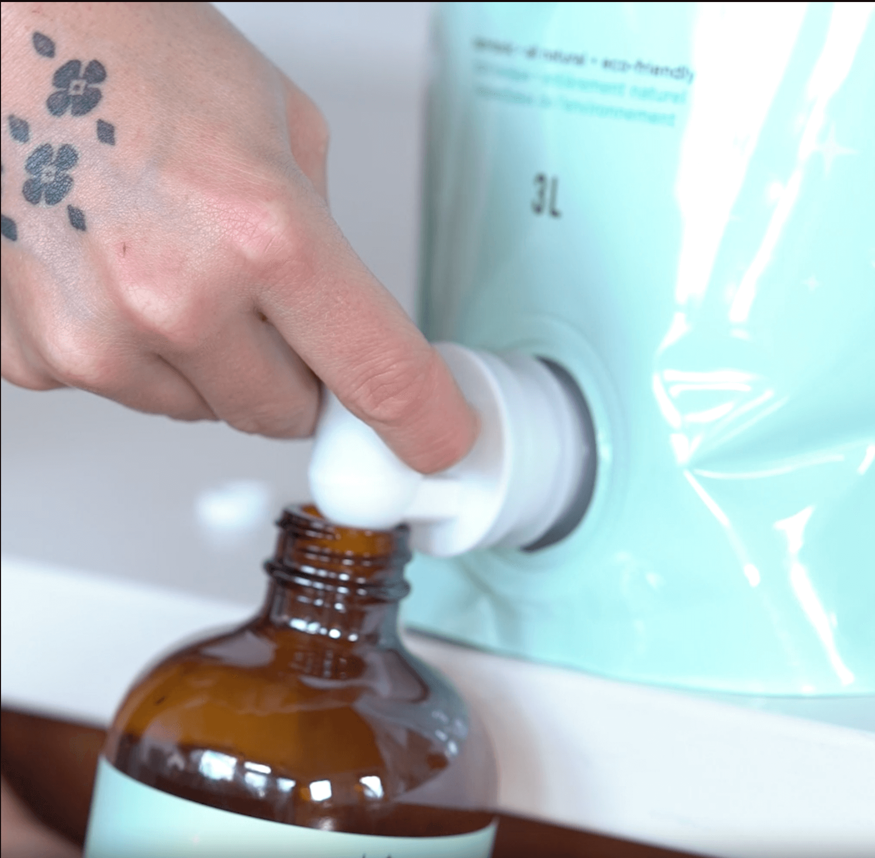 A person refills a hand soap bottle using a Mint Cleaning Products hand soap party pouch, demonstrating an easy and sustainable refill process.