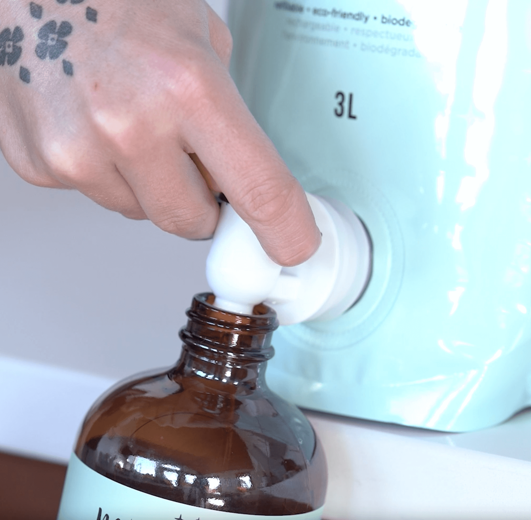 A person refills a Mint dish soap bottle using a Mint dish soap refill, showcasing a simple and eco-conscious refill process.