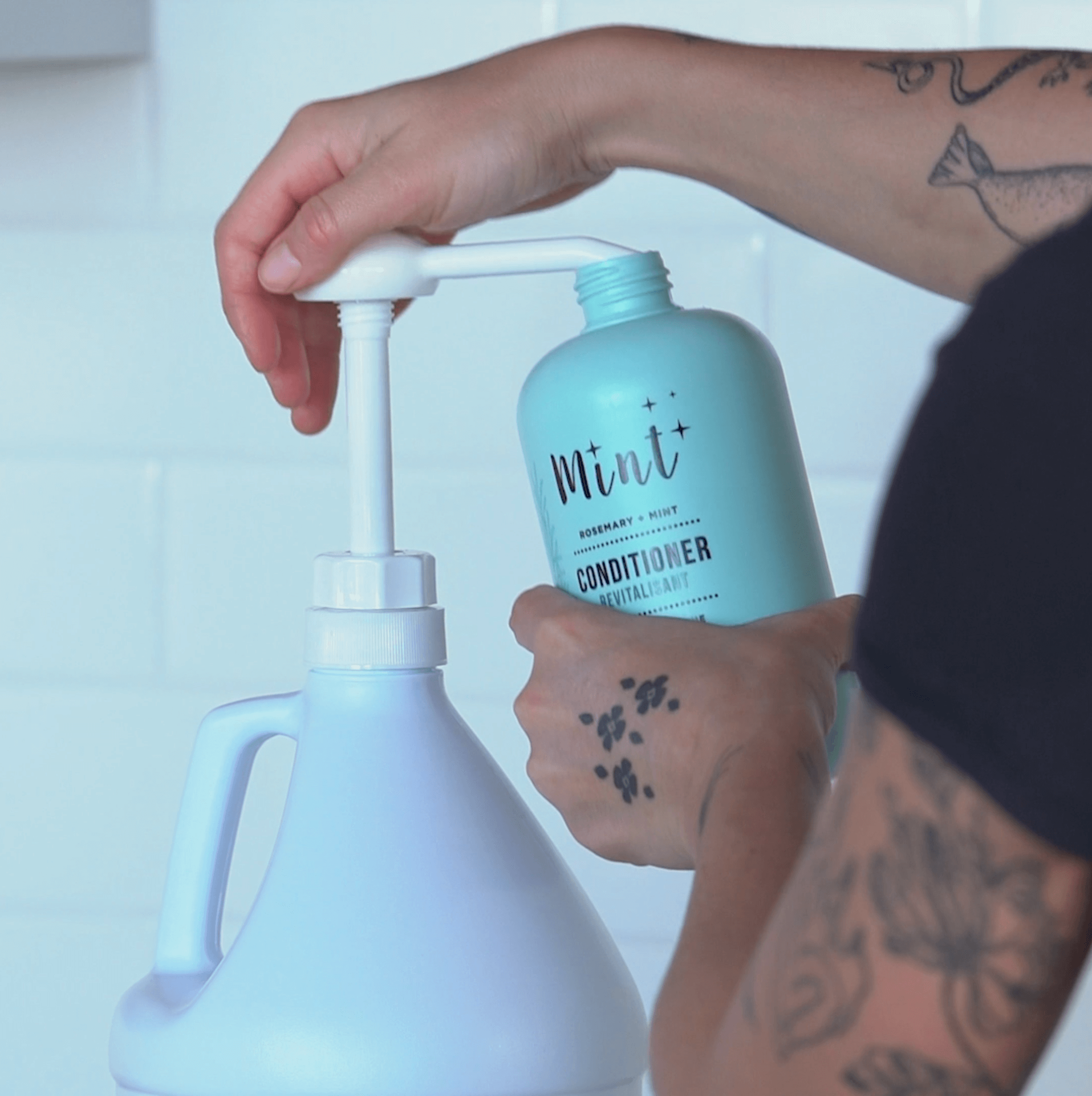 A person refills a Mint conditioner bottle using a Mint conditioner refill jug with a pump dispenser, showcasing an easy and sustainable refill process.