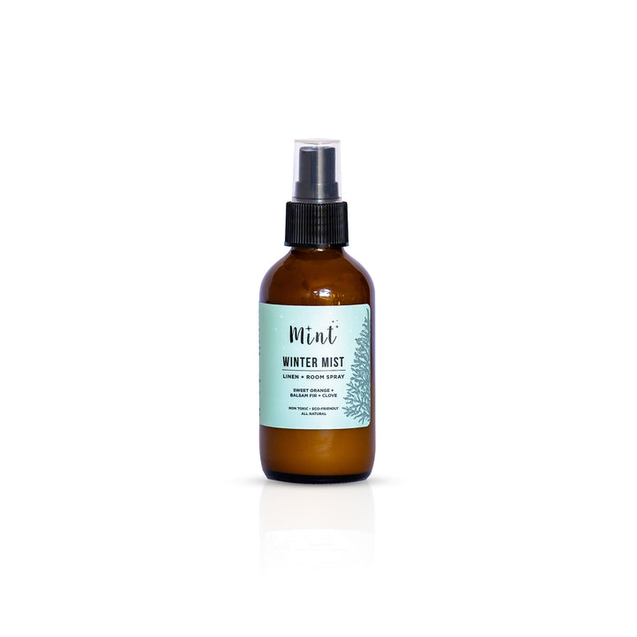 Mint Winter Mist Linen + Room Spray bottle isolated on a white background, highlighting the product label with ingredients like sweet orange, balsam fir, and clove.